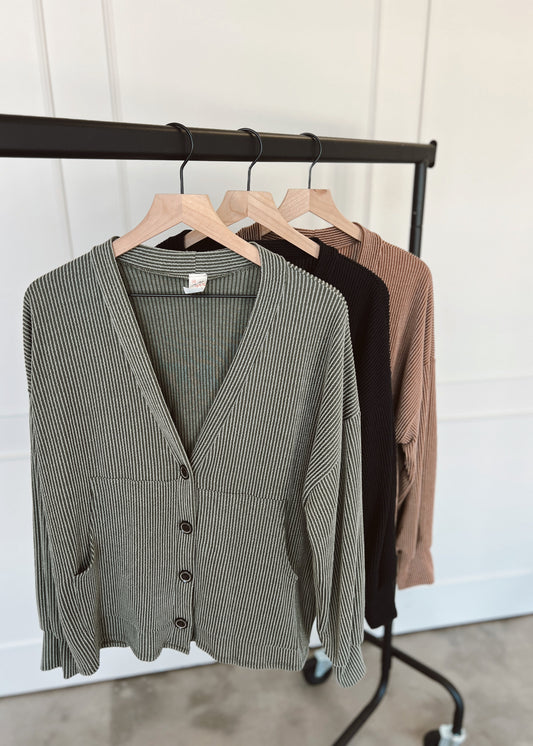 Green cardigan on a rack with other clothing items against a white wall