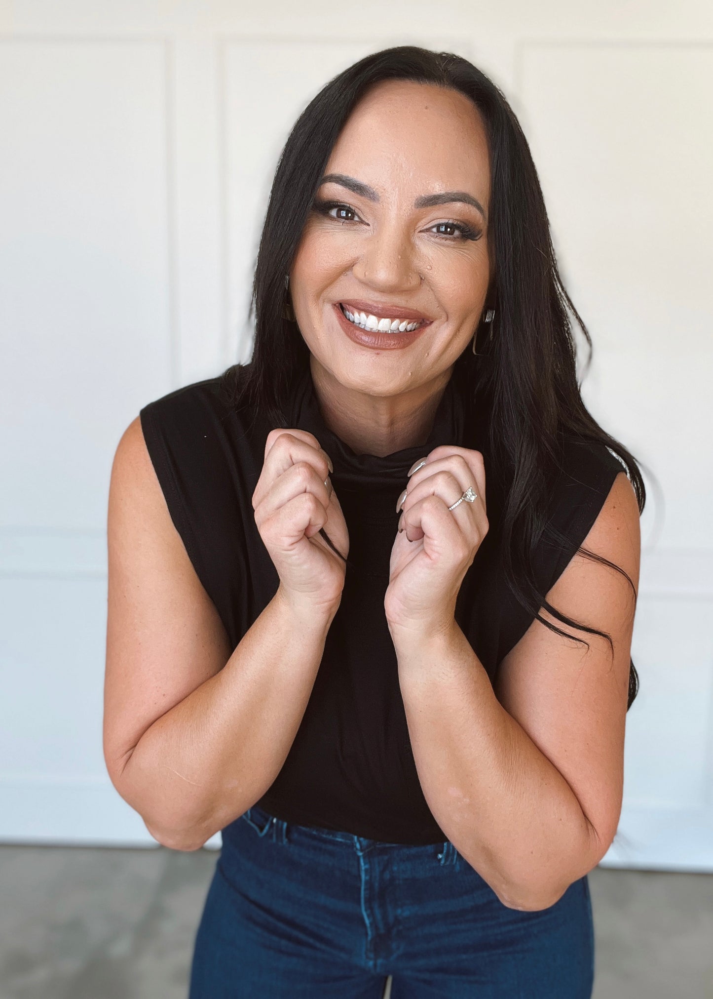 Woman wearing a black sleeveless top and blue jeans with a plain background