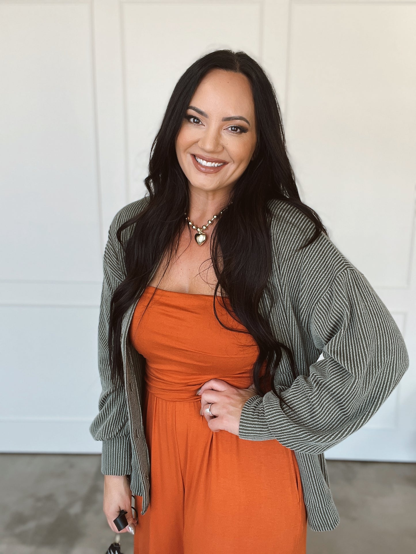 Woman wearing an orange dress and gray cardigan against a white background