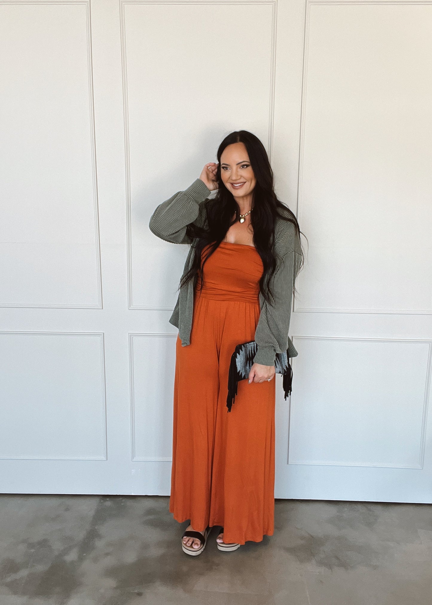 Woman wearing an orange dress and green cardigan against a white paneled wall.