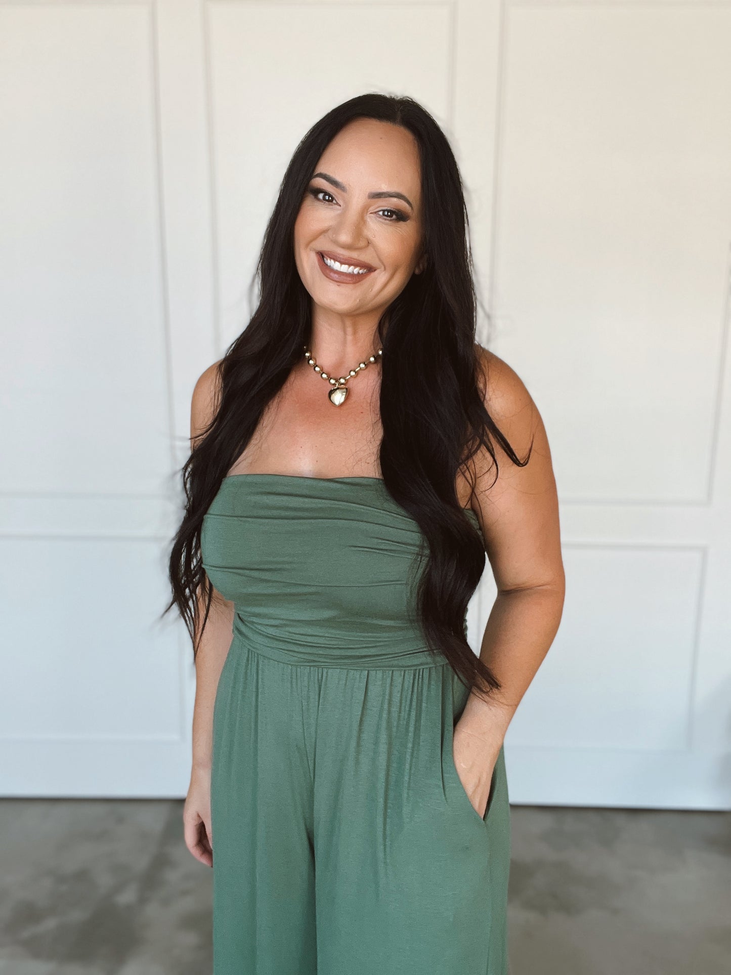 Woman wearing a green strapless jumpsuit standing against a white wall.