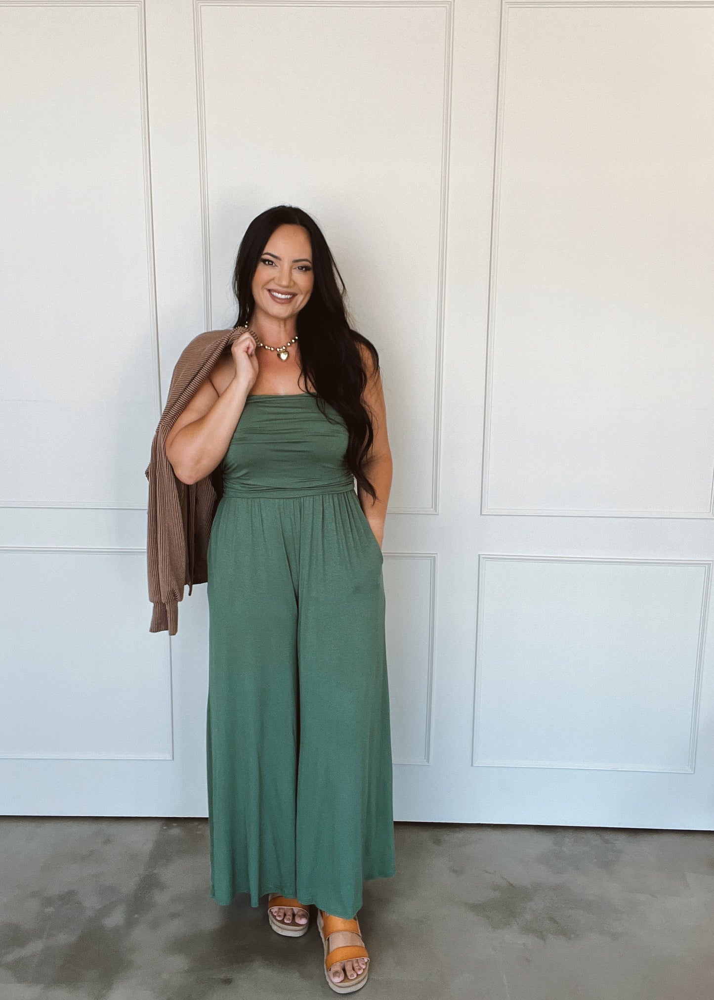 Woman wearing a green jumpsuit standing against a white paneled wall.