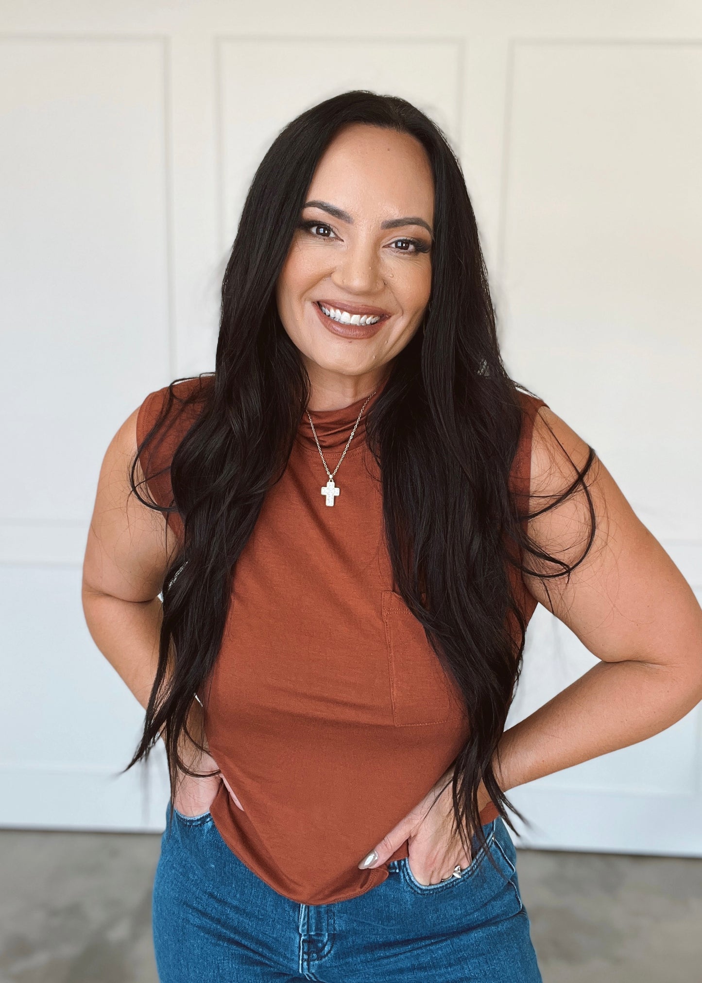 Woman wearing a brown tank top and blue jeans with a white background