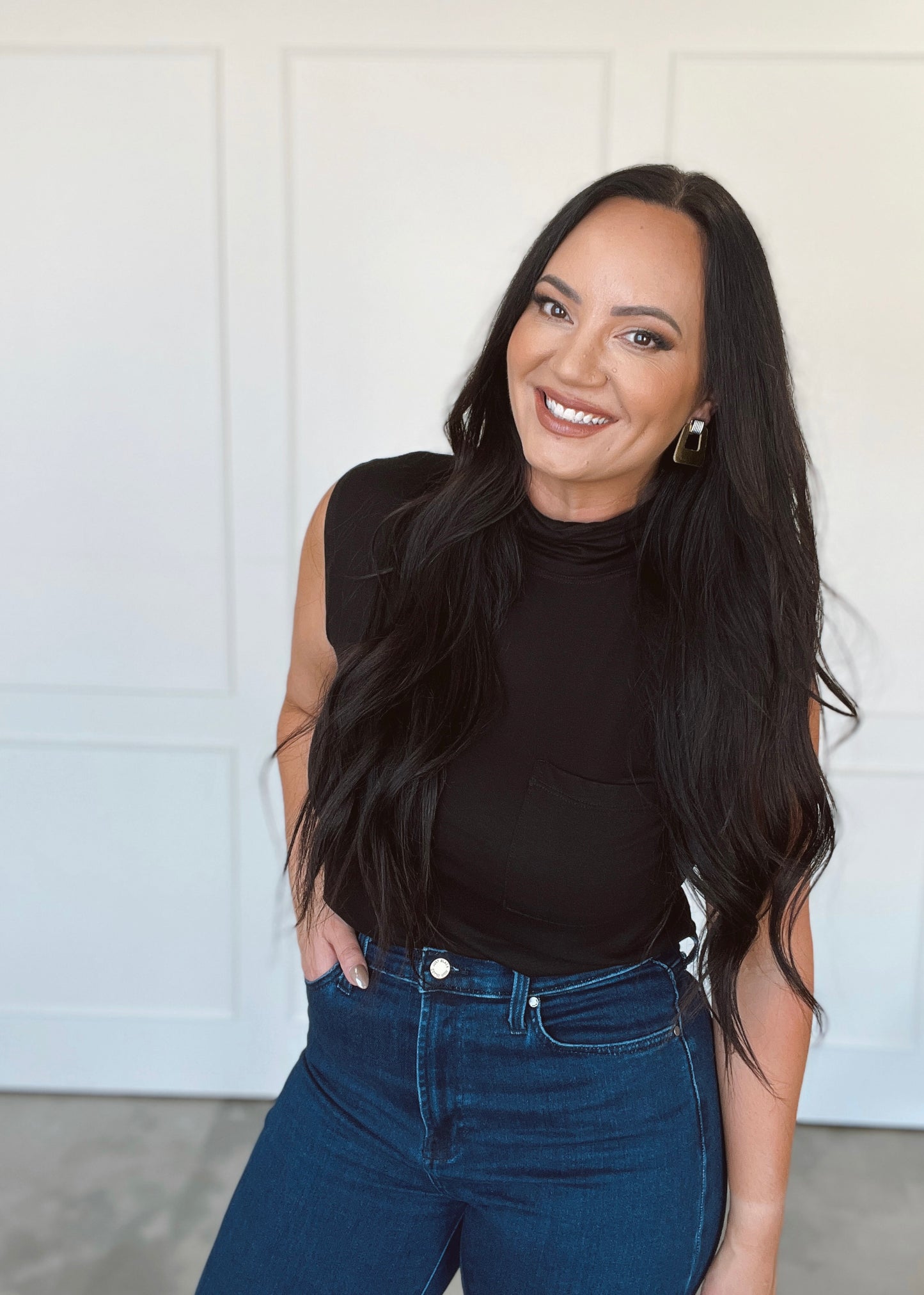 Woman wearing a black sleeveless top and blue jeans against a white background