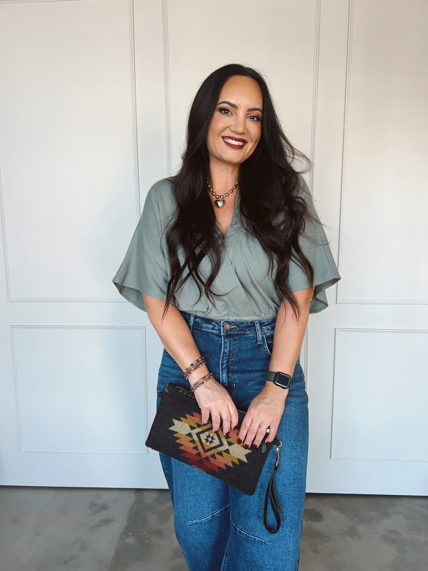 Woman holding a patterned clutch in front of a white paneled wall