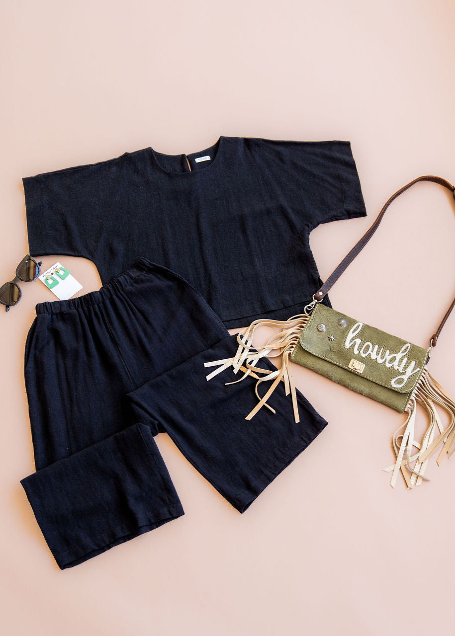Black outfit with a green bag labeled 'howdy' on a beige background