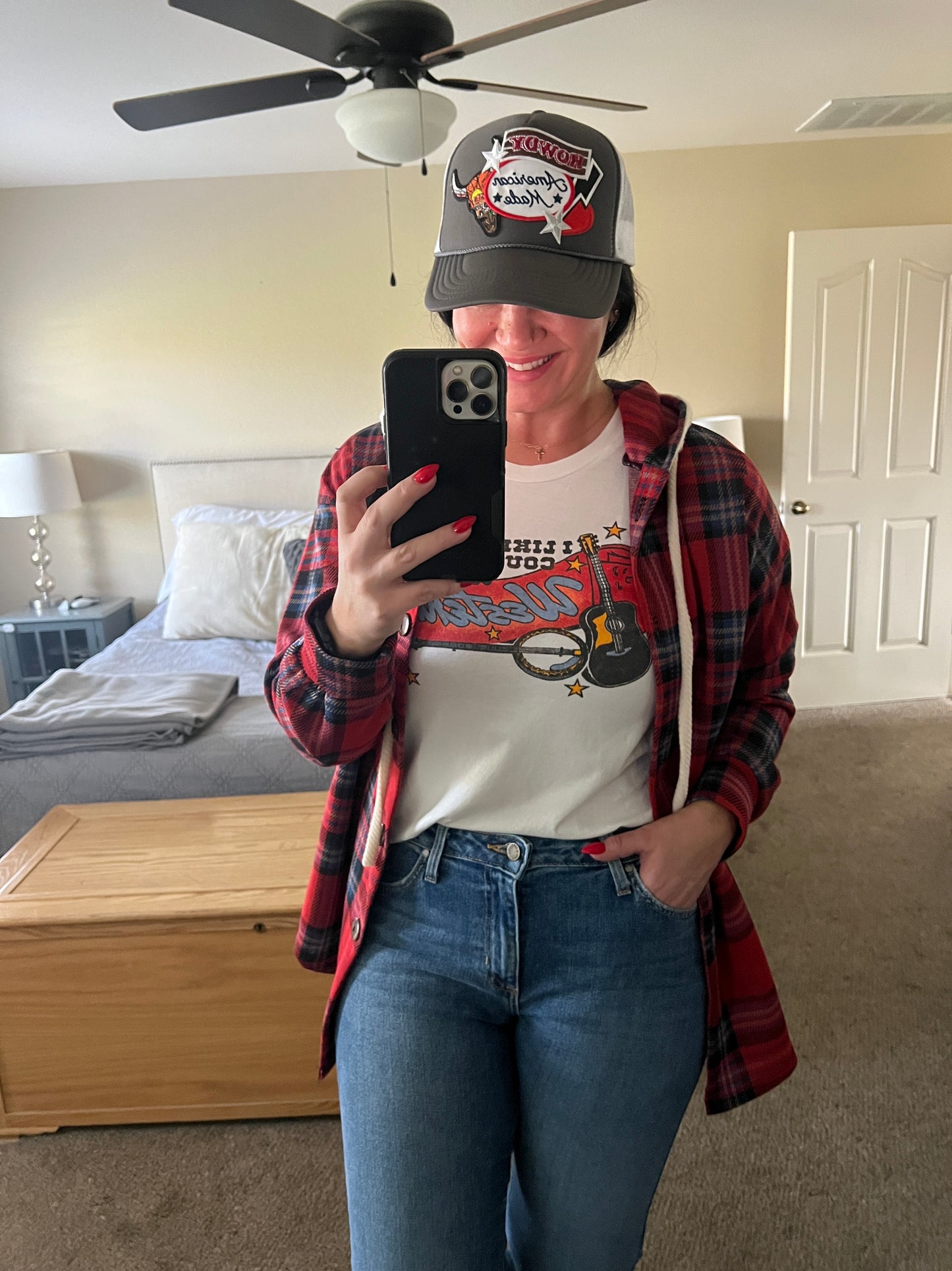 Person wearing a plaid shirt and baseball cap, holding a phone in a room with a ceiling fan.