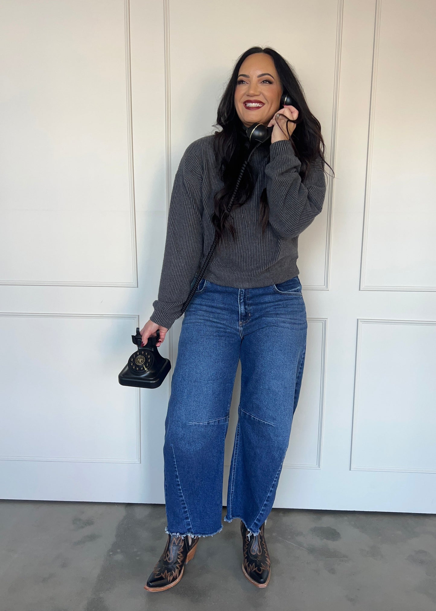 Person wearing a gray sweatshirt and blue jeans standing against a white door.