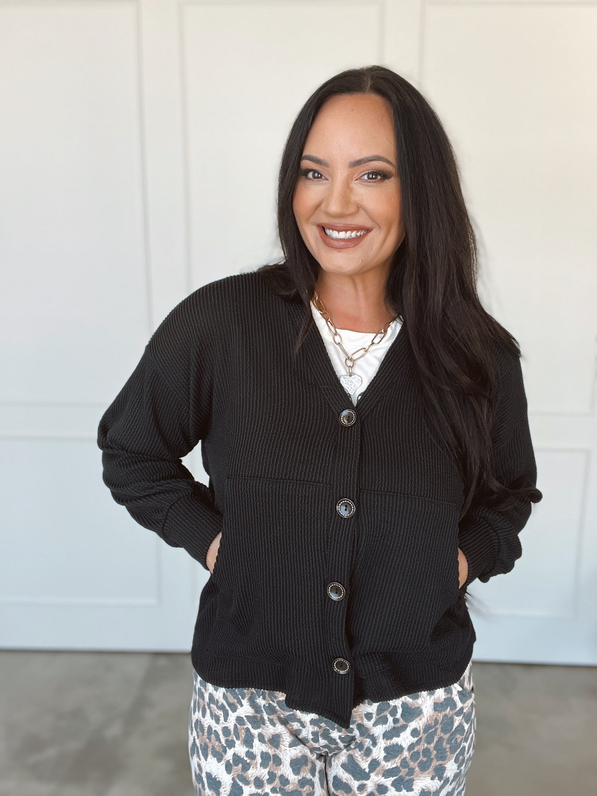 Woman wearing a black cardigan over a patterned top with a white background