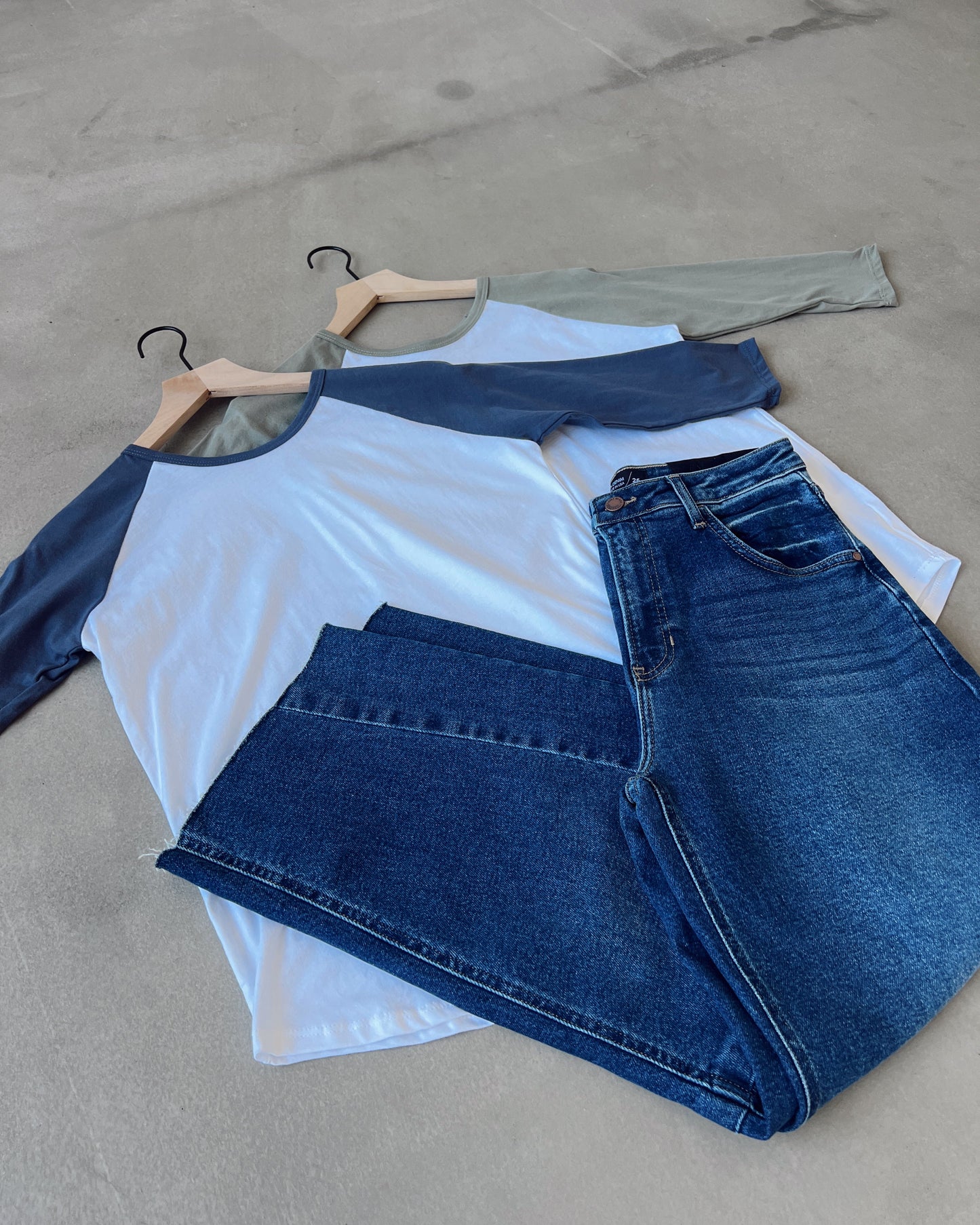 Folded blue jeans and white shirt on a concrete floor with hangers.