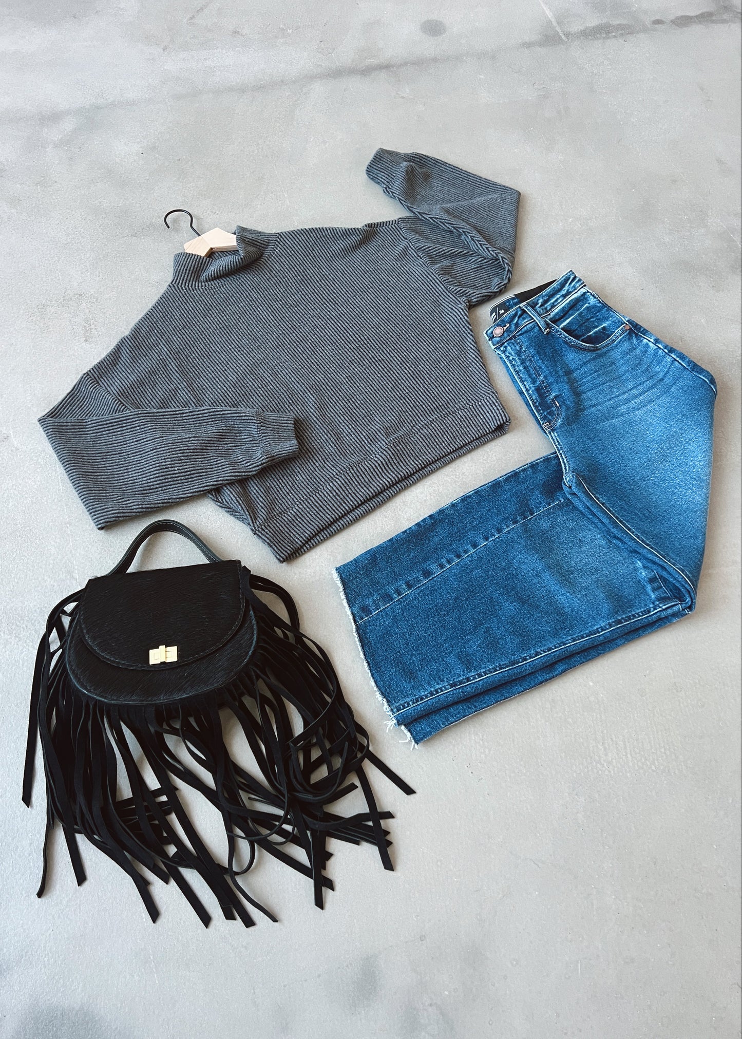 Gray sweater, blue jeans, and black fringed bag on a light gray surface
