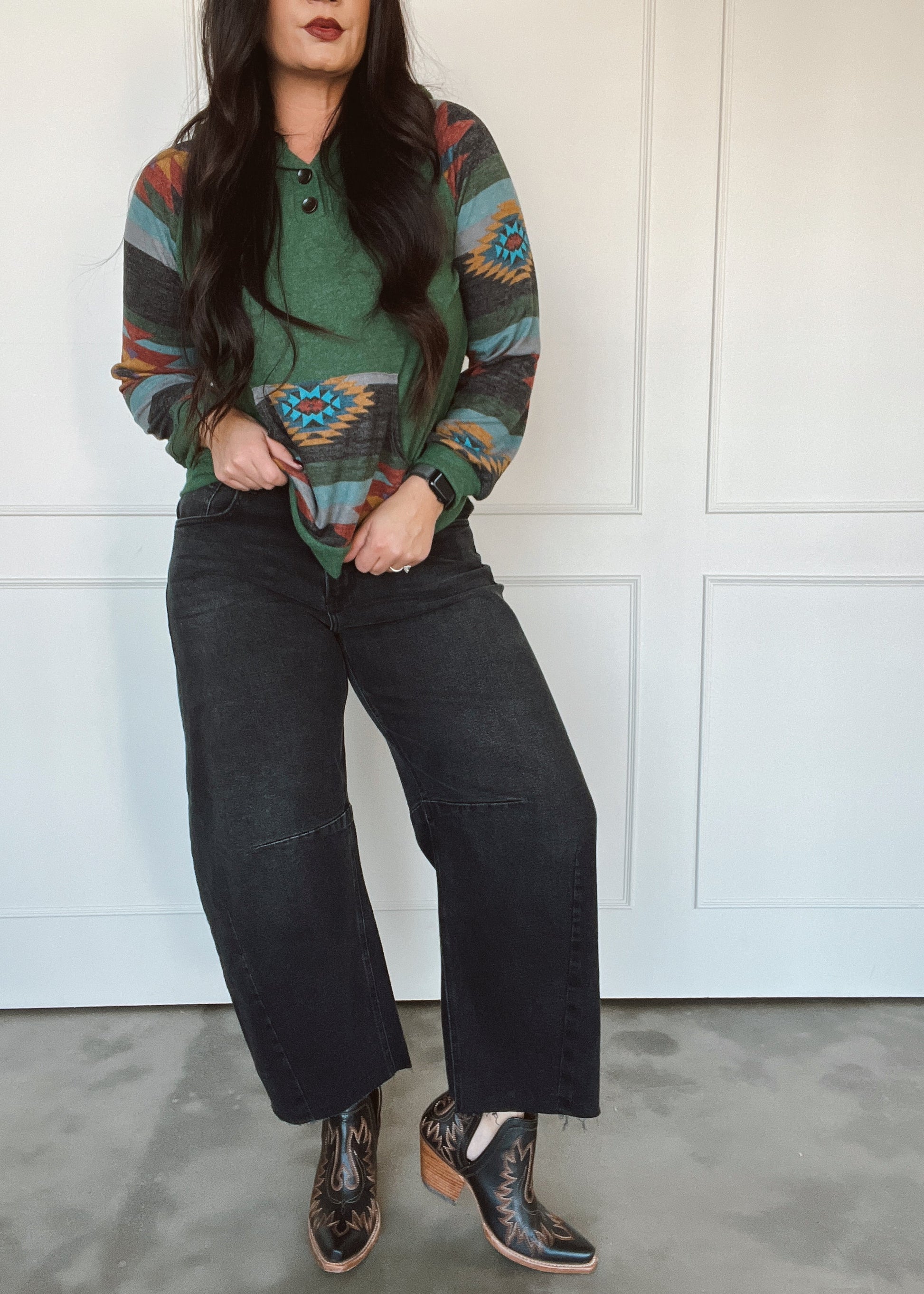 Person wearing a patterned sweater, black pants, and brown boots against a white wall.