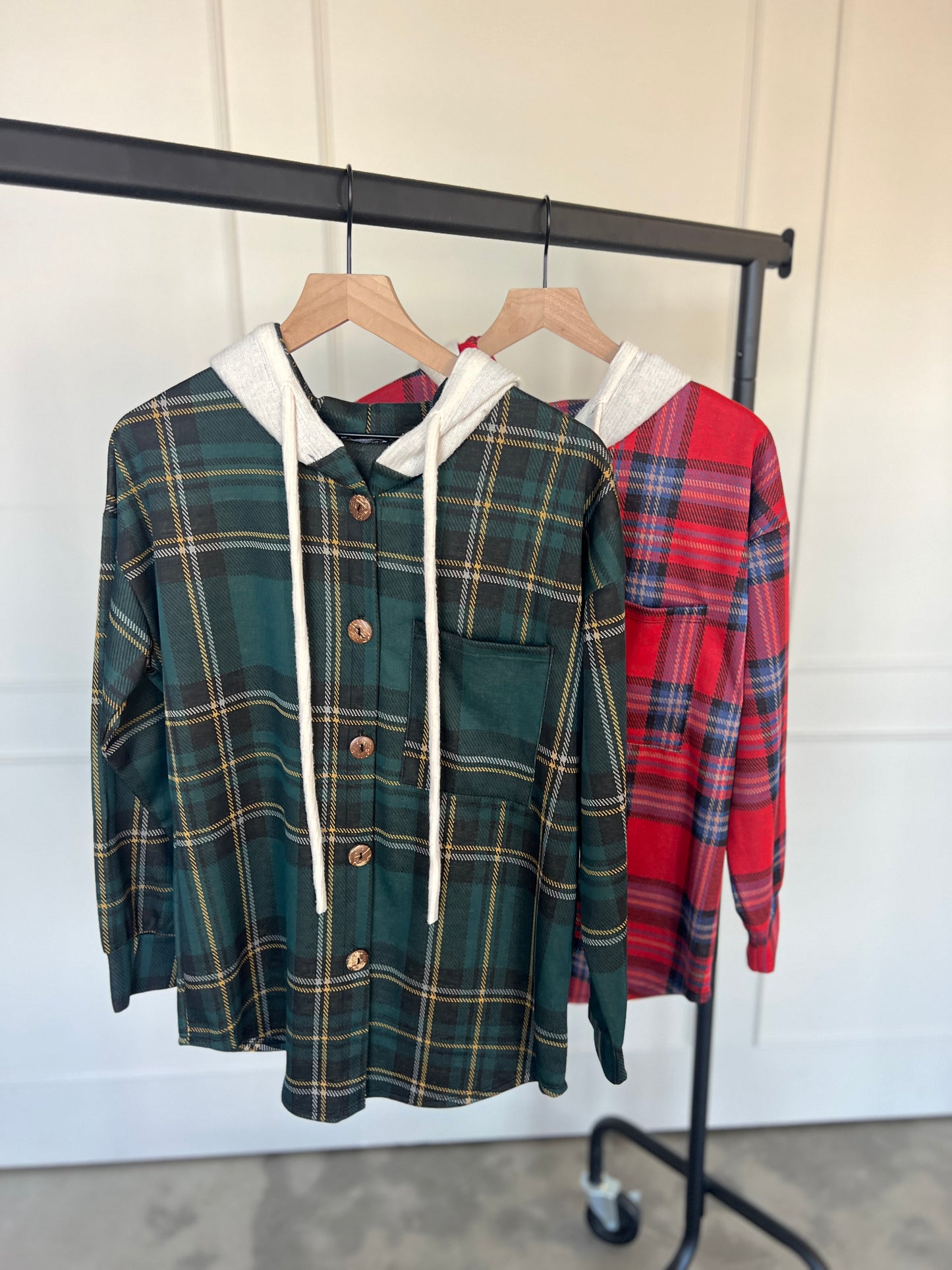 Two plaid shirts, one green and one red, hanging on a rack against a white wall.