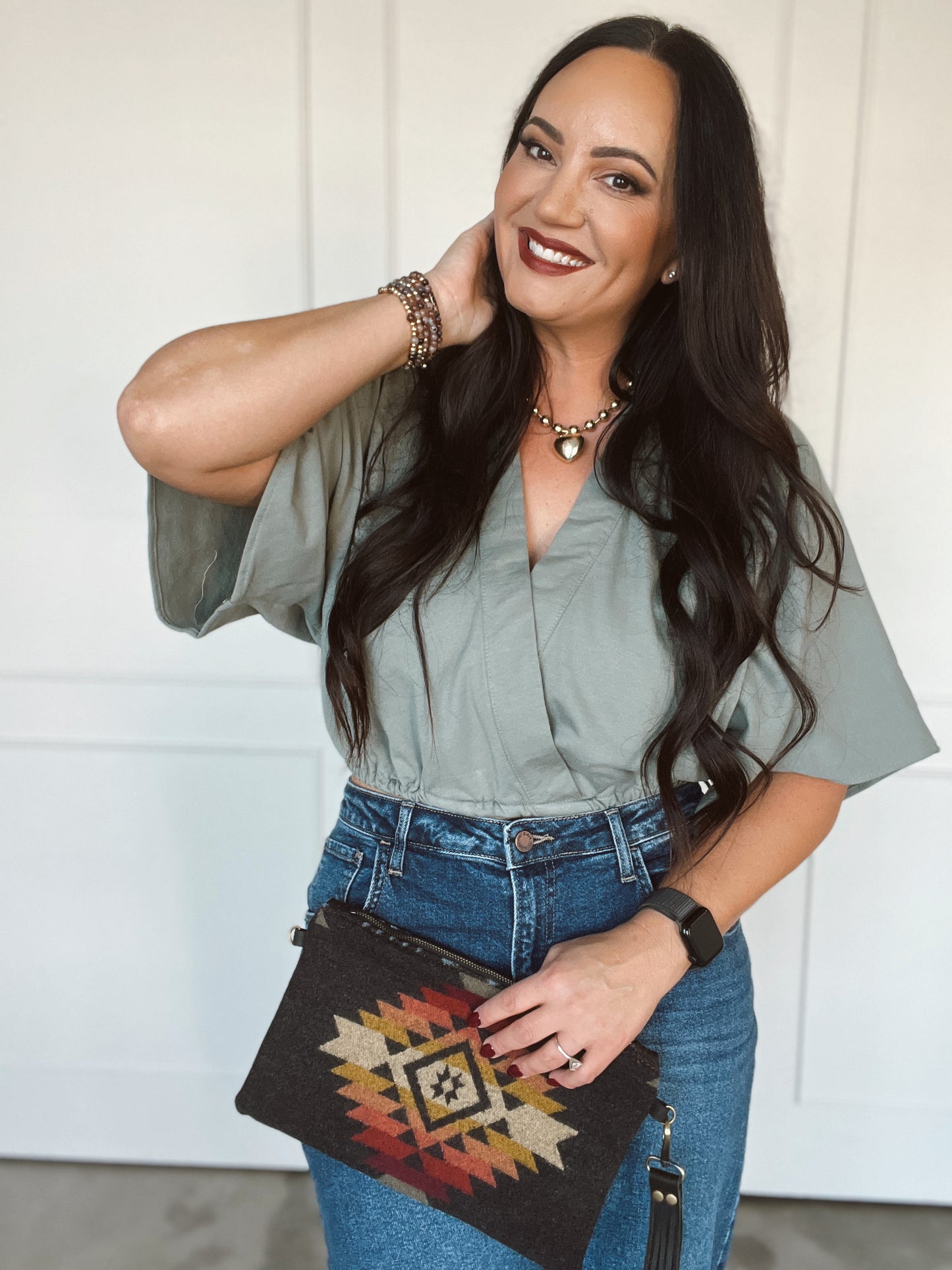 Woman wearing a green blouse and blue jeans, holding a patterned clutch.
