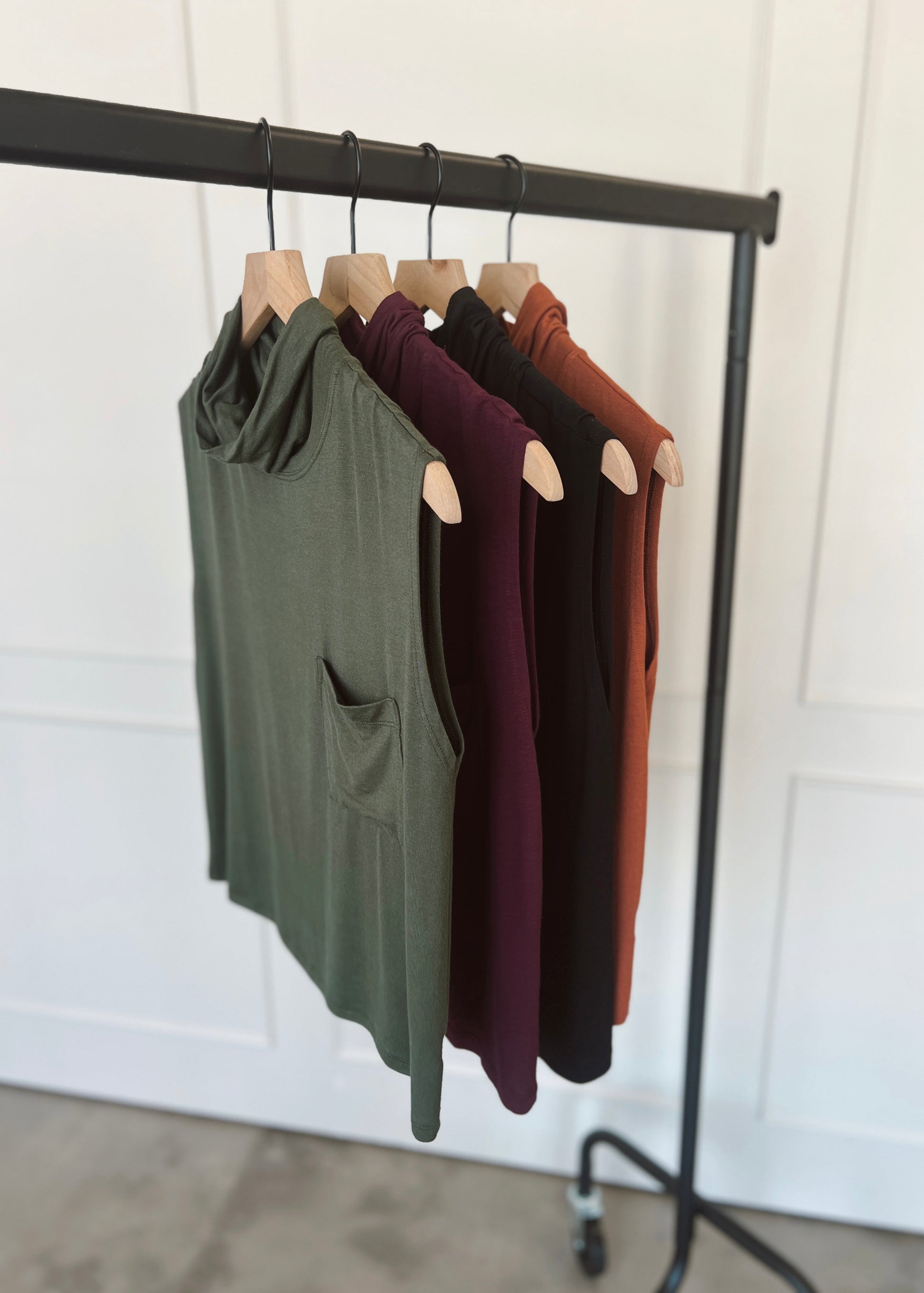 Four tank tops in green, purple, and brown hanging on a rack against a white wall.