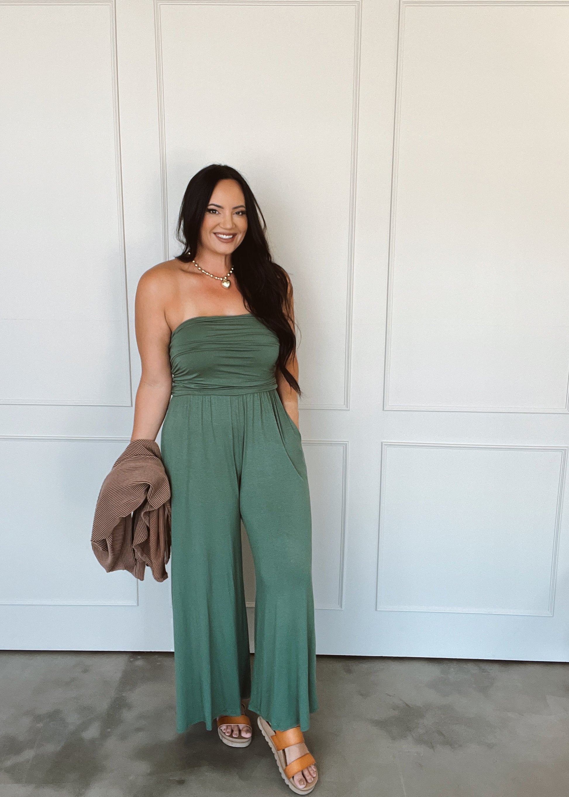 Woman wearing a green strapless jumpsuit standing against a white paneled wall.